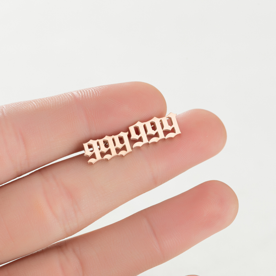 Gold-tone 999 Whispered Number stud earrings shown on fingers for visual scale