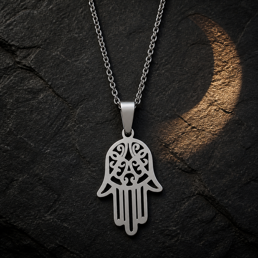The Open Hand silver necklace on dark slate with crescent-shaped warm light